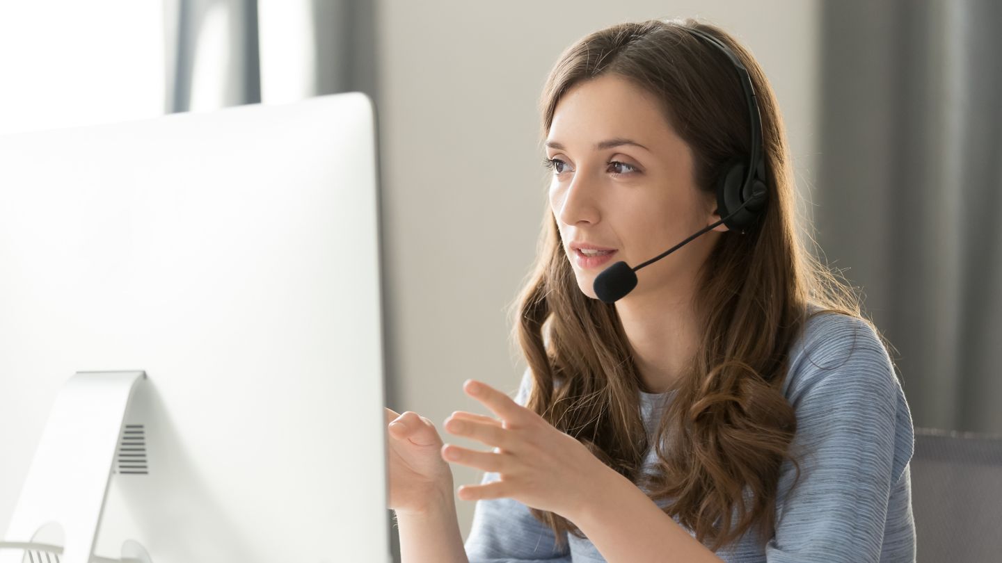 Serious call center operator in wireless headset talking with customer, woman in headphones with microphone consulting client on phone in customer support service, looking at computer screen close up