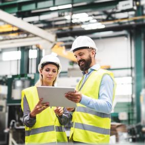 A portrait of a mature industrial man and woman engineer with tablet in a factory, talking.
