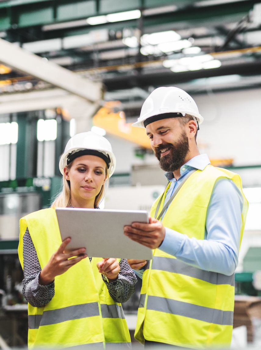 A portrait of a mature industrial man and woman engineer with tablet in a factory, talking.